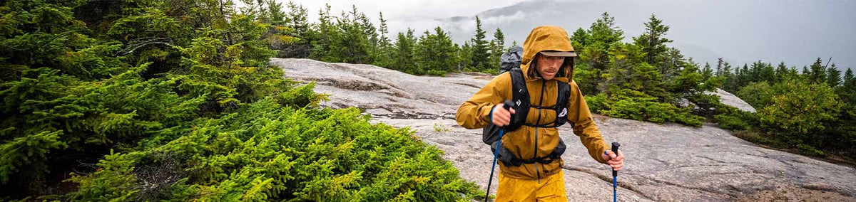 Man in yellow hooded coat trekking with poles outdoors