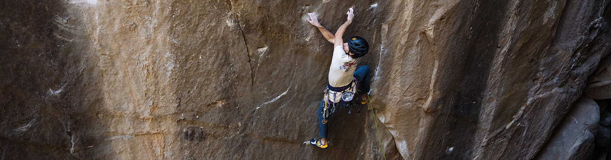 Man wearing climbing helmet and blue hoodie rock climbing outdoors