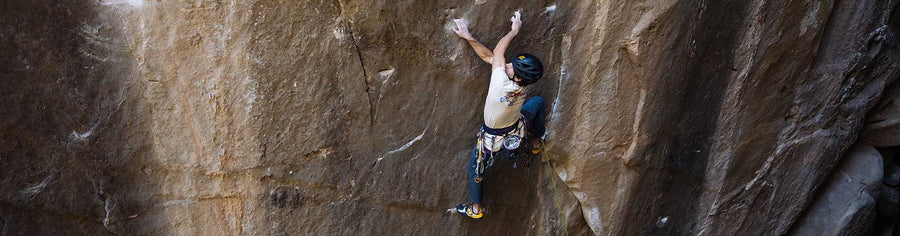 Man wearing climbing helmet and blue hoodie rock climbing outdoors