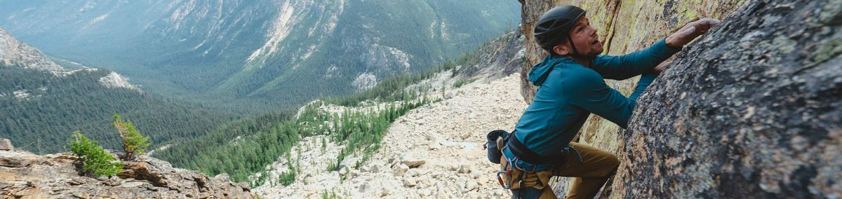 Man wearing climbing helmet and blue hoodie rock climbing outdoors