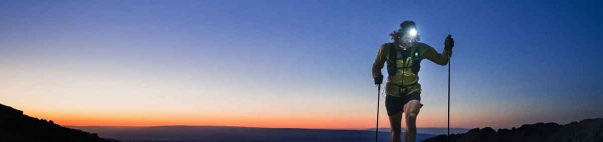 Person hiking at dusk with the assistance of hiking poles and headlamp
