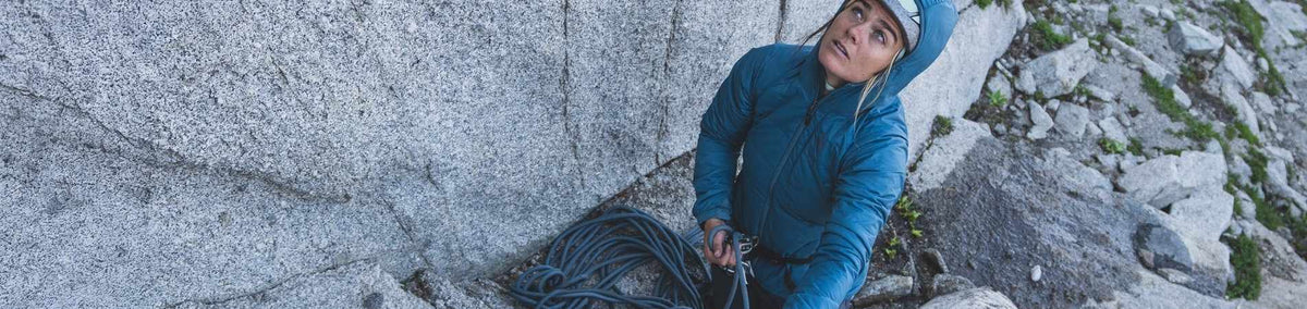Woman in complete climbing apparel looking up to inspect rock wall outdoors