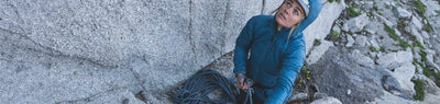 Woman in complete climbing apparel looking up to inspect rock wall outdoors