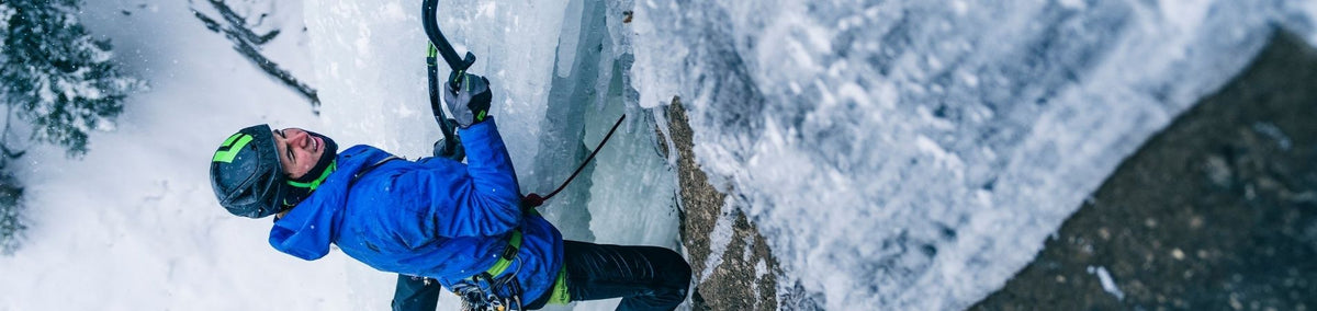 Man climbing up frozen ice wall in full climbing gear with ice axe in hand