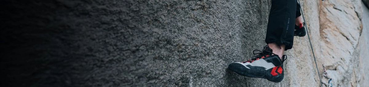 Woman climbing outdoors wearing black climbing shoes with crash pads underneath
