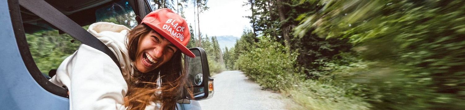 Woman in red hat with BLACK DIAMOND branding smiling with head outside of car