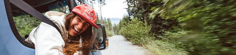 Woman in red hat with BLACK DIAMOND branding smiling with head outside of car