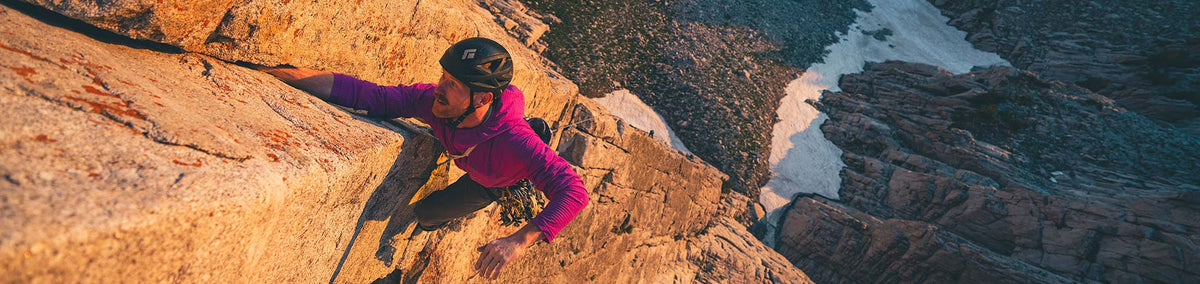 Man in pink fleece jacket climbing cliff
