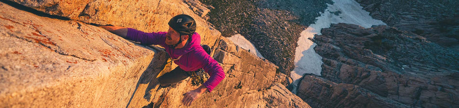 Man in pink fleece jacket climbing cliff