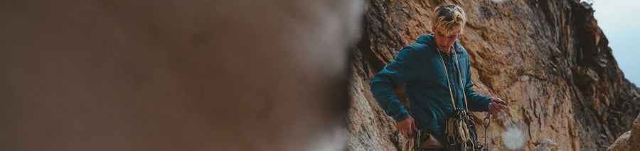 Man in blue insulated jacket standing in front of rock face