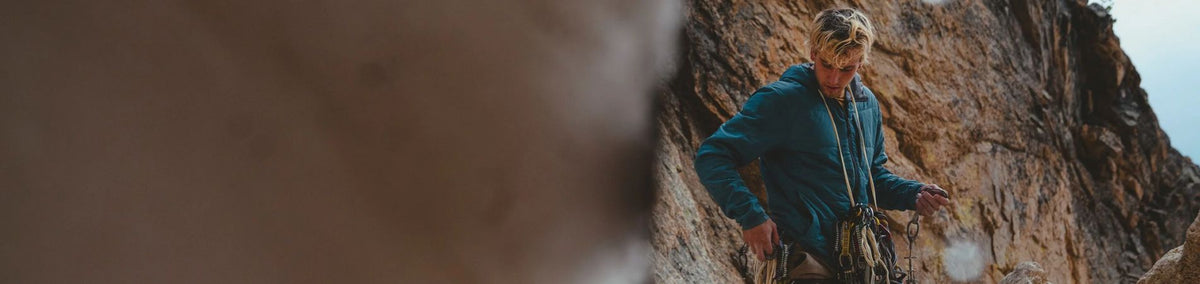 Man in blue insulated jacket standing in front of rock face