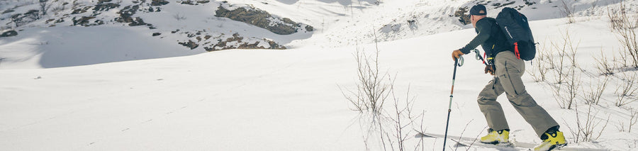 Man wearing beige shell pants trekking through the snow in full snow gear