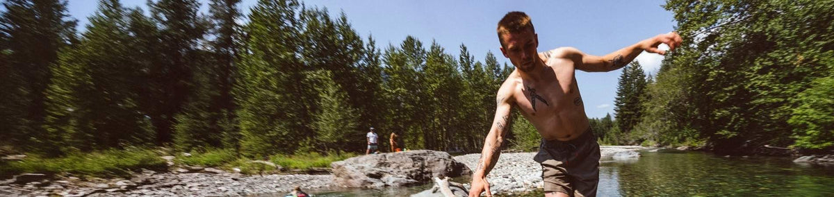 Shirtless man balancing across a river