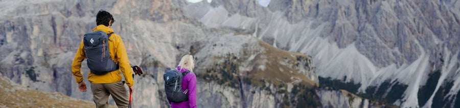 Two people hiking down mountain wearing hiking packs