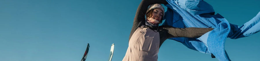 A woman throwing on a blue insulated jacket to keep warm in the cold