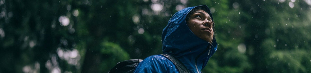Close-up of a durable women's rain jacket in blue, showcasing its hood and water repellency, ideal for outdoor adventures in wet weather