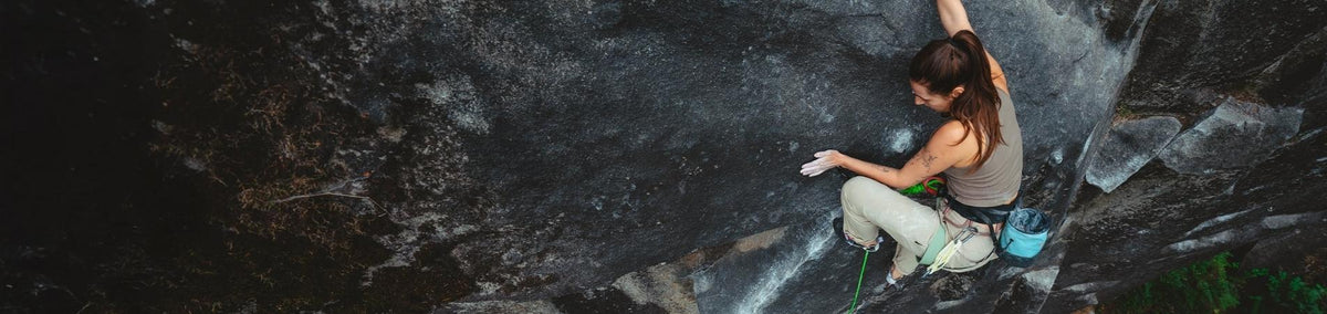 Woman wearing climbing gear climbing up a rock wall outside