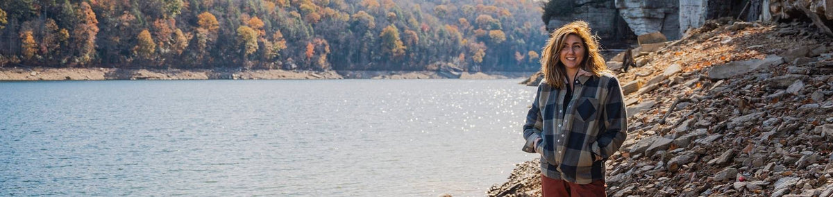 Woman standing on the edge of a lake wearing a flannel shirt