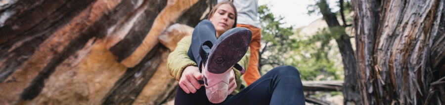 Woman putting on climbing shoes with rock wall background outdoors