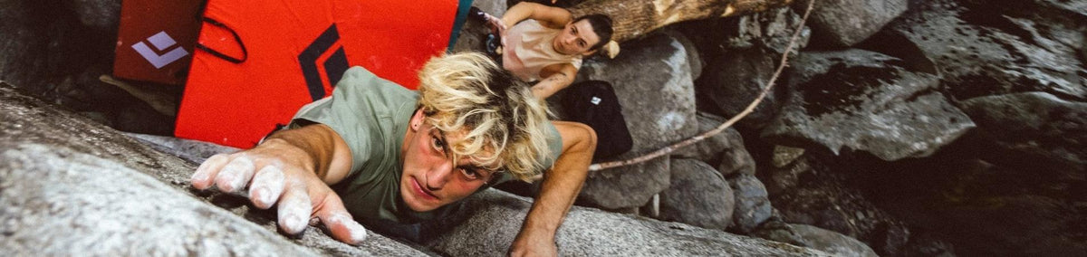 Man climbing rock wall outdoors with bouldering pads underneath