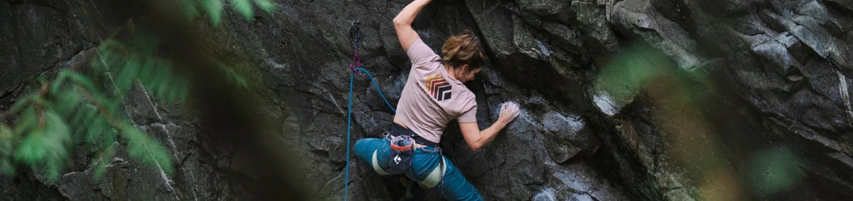 Woman in a harness and pink shirt climbing a cliff