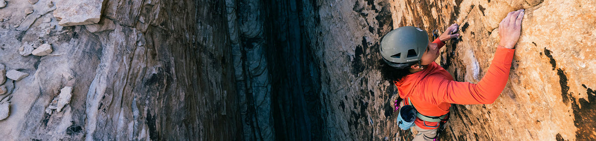 Man climbing rockwall outdoors with Black Diamond crash pads underneath